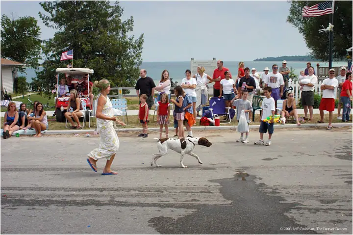 Woman leads a spotted dog past spectators and flags during an outdoor community celebration.