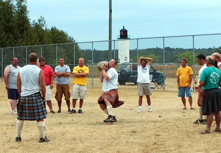 A man holds a large stone during an outdoor throwing event as others watch.