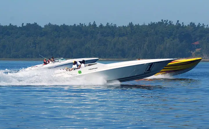 Two high-performance motorboats race across the water, throwing up broad wakes in front of a wooded shoreline.