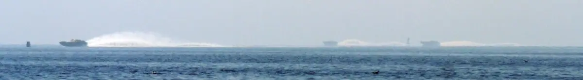 Several fast boats race across open water, throwing up broad white wakes.