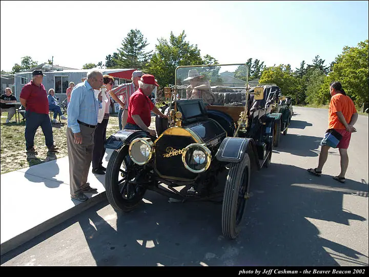 A vintage open automobile is displayed on a paved street as several people look it over.