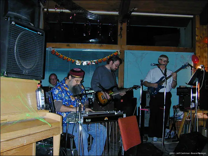 Four musicians perform indoors beneath a HAPPY HALLOWEEN banner.
