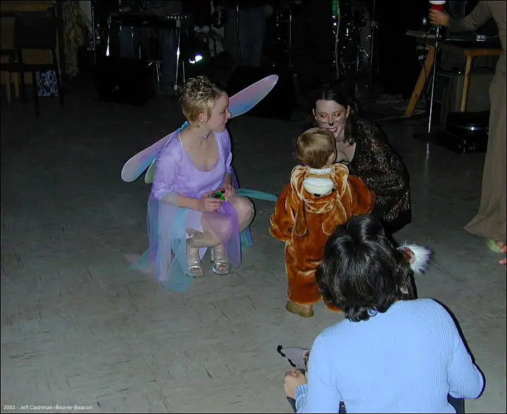 People in costumes gather around a child on a dance floor during a party.