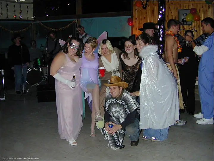 Costumed people pose together at a decorated party with balloons, drinks, and musical equipment.