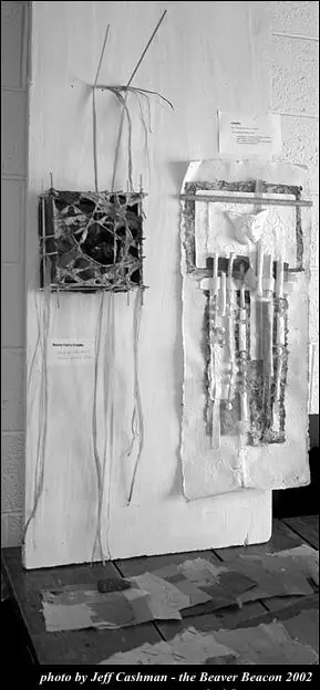 Two abstract paper sculptures with tangled fibers, relief forms, and dangling strips are displayed on a gallery wall.