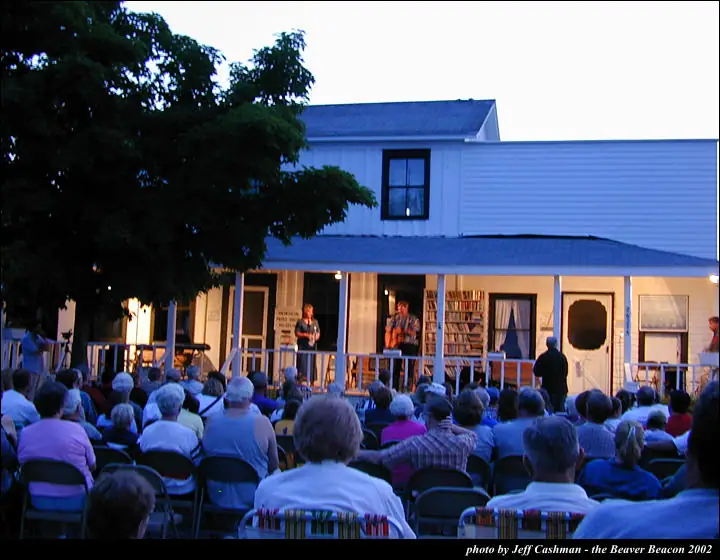 Evening music performance on a porch before a seated outdoor audience.
