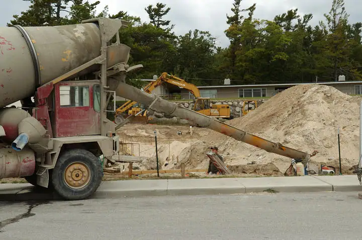 A concrete mixer truck pours material through a chute at a construction site beside an excavator.