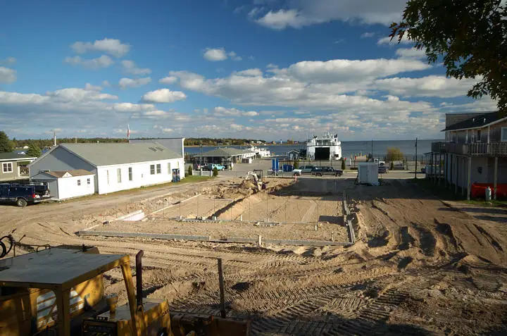 A concrete foundation is under construction beside a waterfront with a docked white vessel.