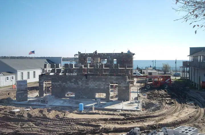 Concrete-block building under construction beside a dirt work area, with a red skid-steer loader.