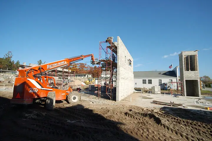Construction equipment beside concrete-block walls and scaffolding under a clear blue sky.