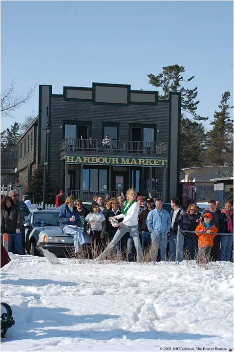 Crowd gathered in snow outside the Harbour Market building, with a woman wearing a green garland at center.