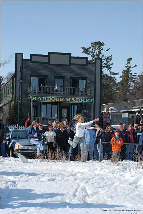 A person leaps in front of a storefront as a crowd watches from behind a fence in the snow.