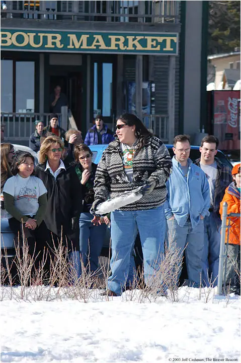 People gather in winter snow outside a storefront while a woman holds a large silvery fish.