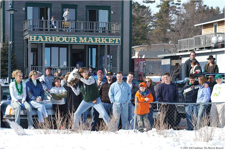 People gather in snowy weather outside a storefront while others watch from a balcony.