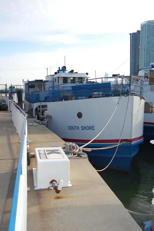 A blue-and-white ferry named SOUTH SHORE is moored beside a concrete pier near tall waterfront buildings.