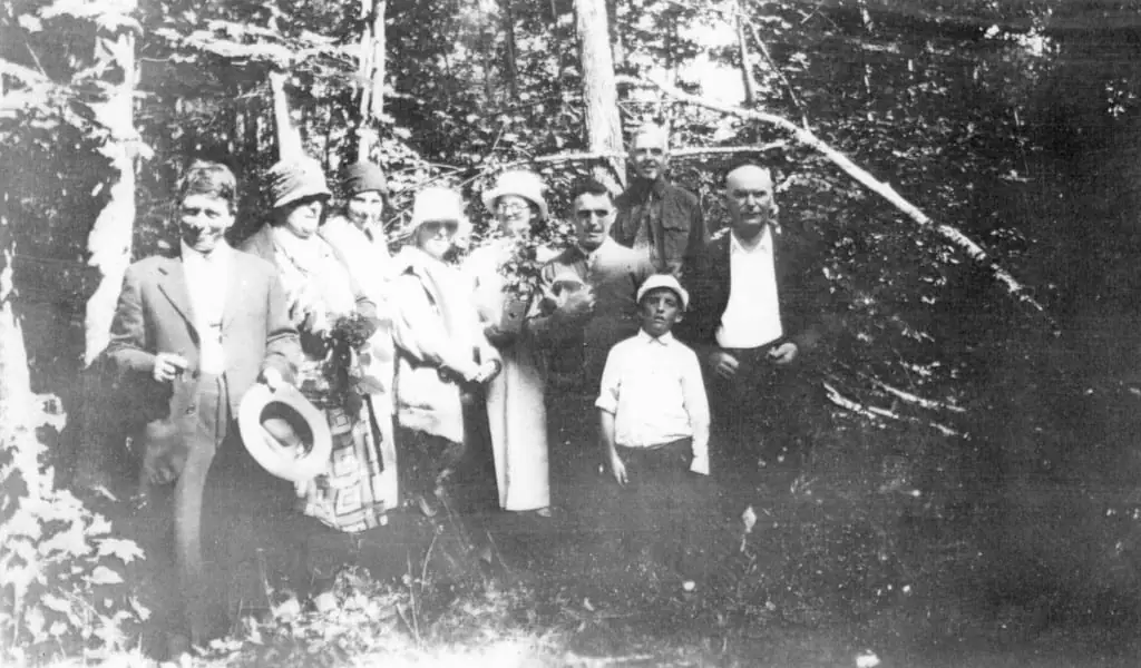 A group of adults and a boy pose among trees, with several wearing hats and coats.