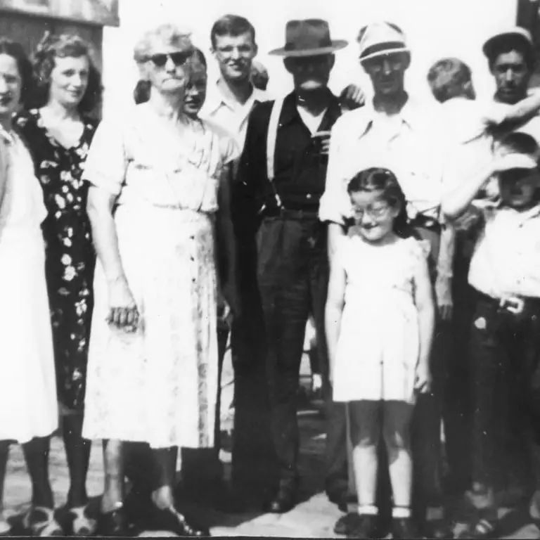 Group portrait of adults and a young girl standing outdoors, with several people wearing hats and sunglasses.