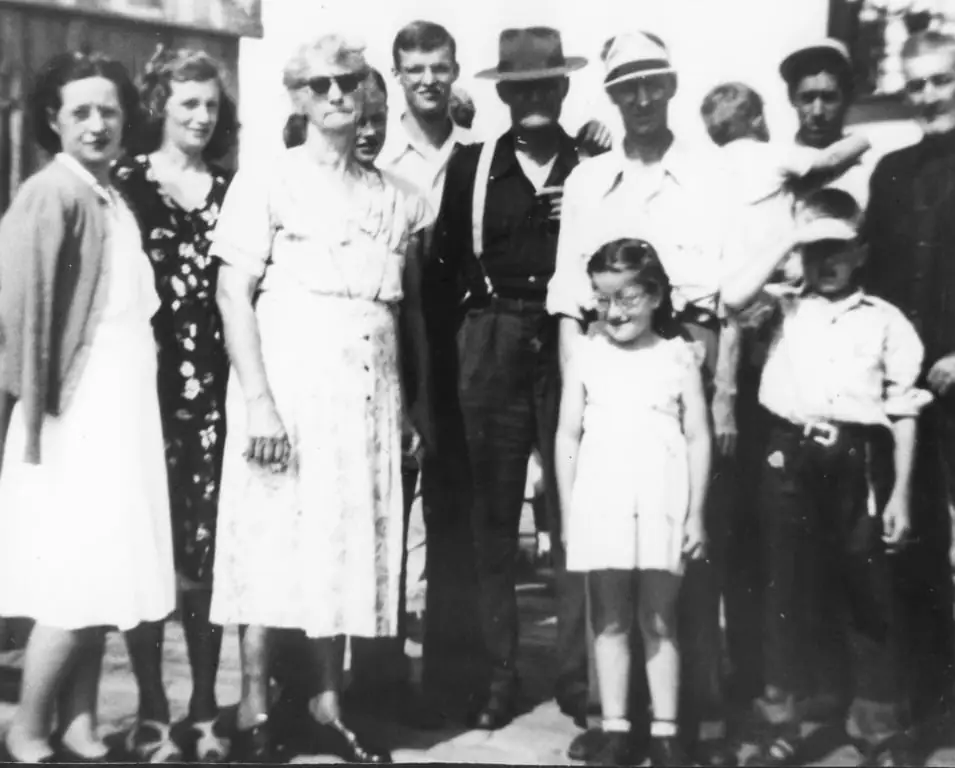 A group of adults and children poses outdoors, with several people wearing hats and one child being held.