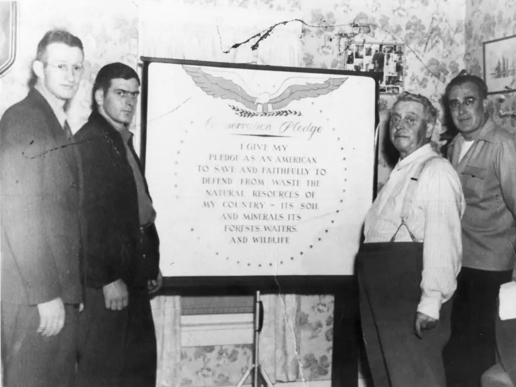Four adults stand around a framed conservation pledge displayed on an easel in an indoor room.