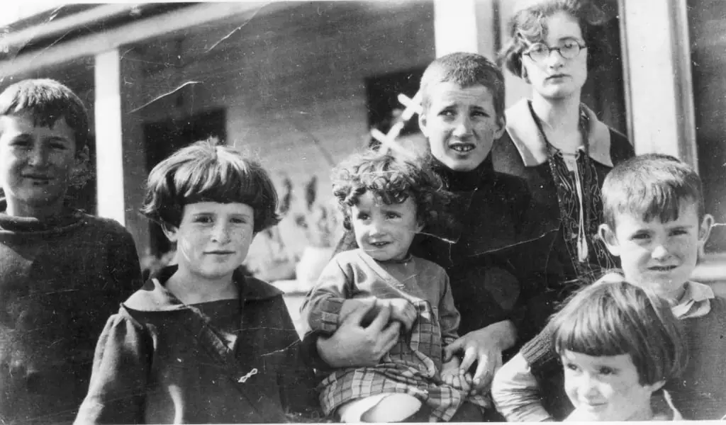 Black-and-white photograph of six children and an adult woman gathered on a porch.