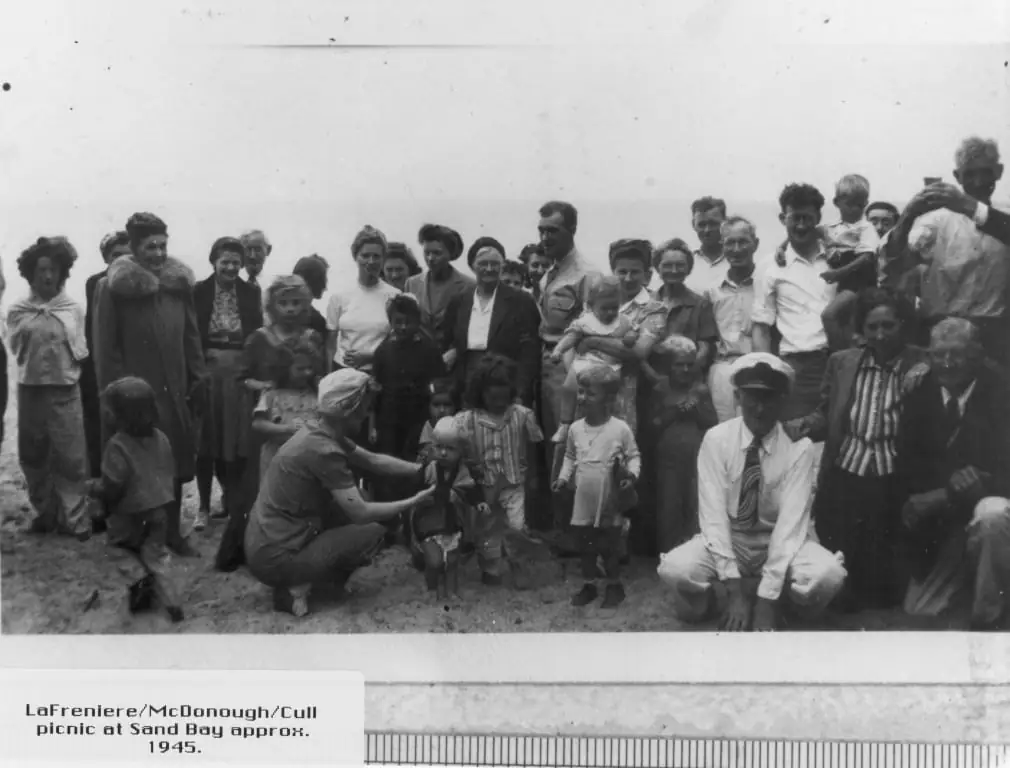 Adults and children pose together on sandy ground in an outdoor group portrait.