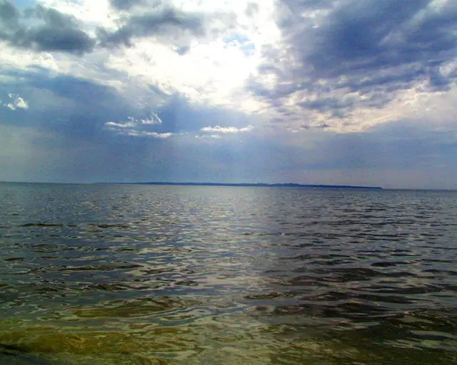 Rippling open water beneath dark storm clouds with sunlight breaking through.