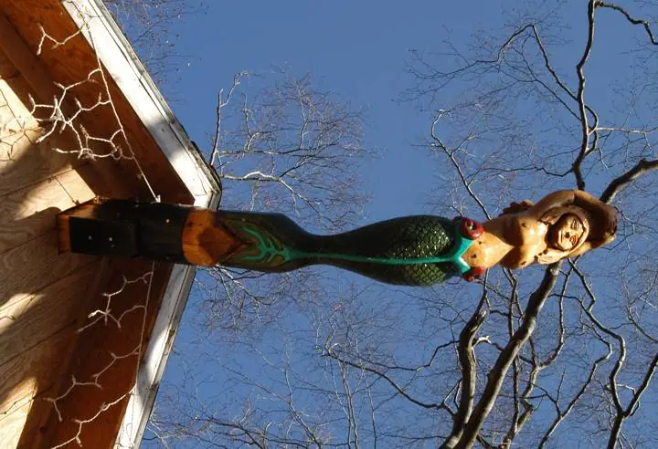 A carved mermaid figure with a green-black tail is mounted on the corner of a wooden building.