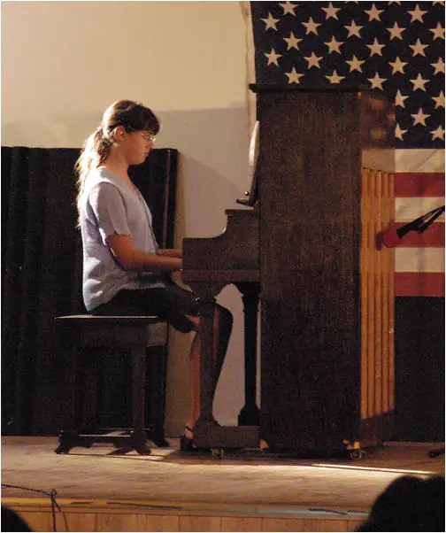 A pianist performs on a grand piano beneath an American flag backdrop.