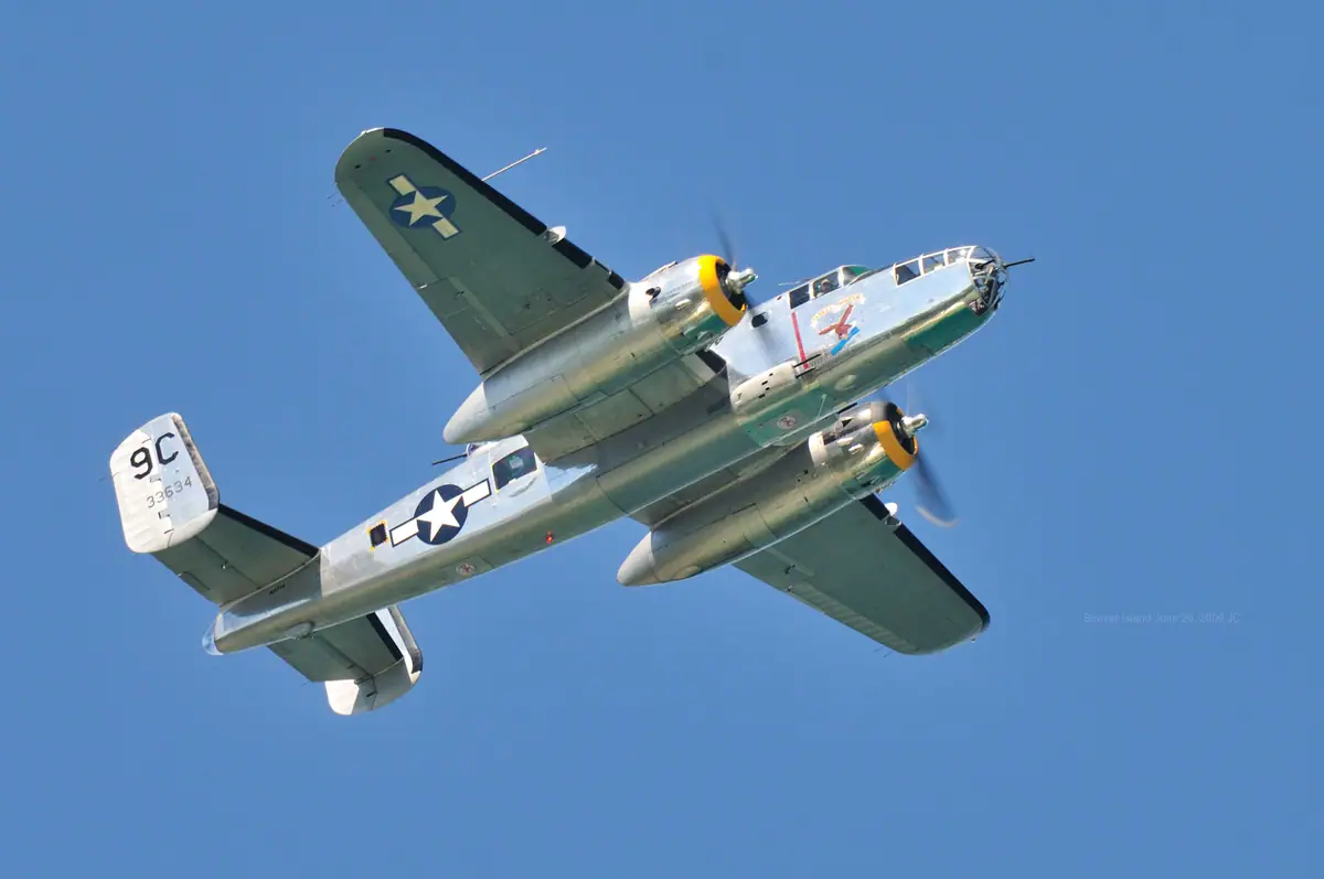 Twin-engine military aircraft flying overhead against a clear blue sky.