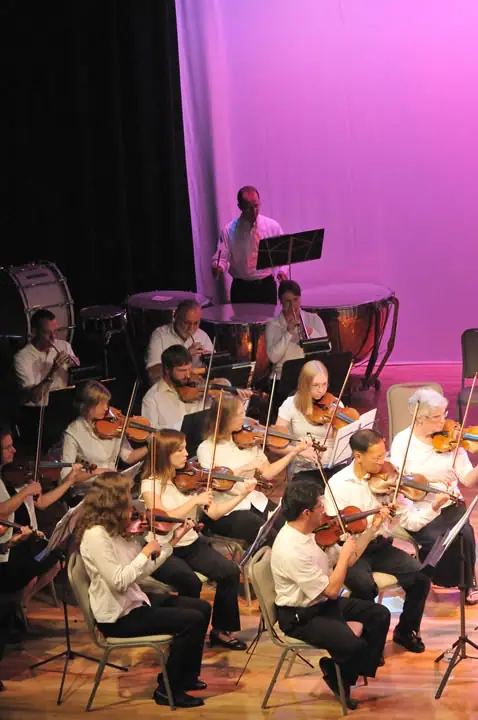 String musicians perform on a brightly lit stage with percussion instruments behind them.