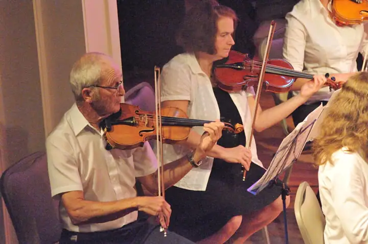 Musicians play violins together while following sheet music.