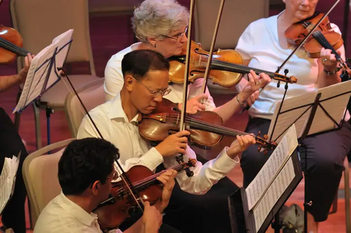 Seated string musicians play violins while reading sheet music.
