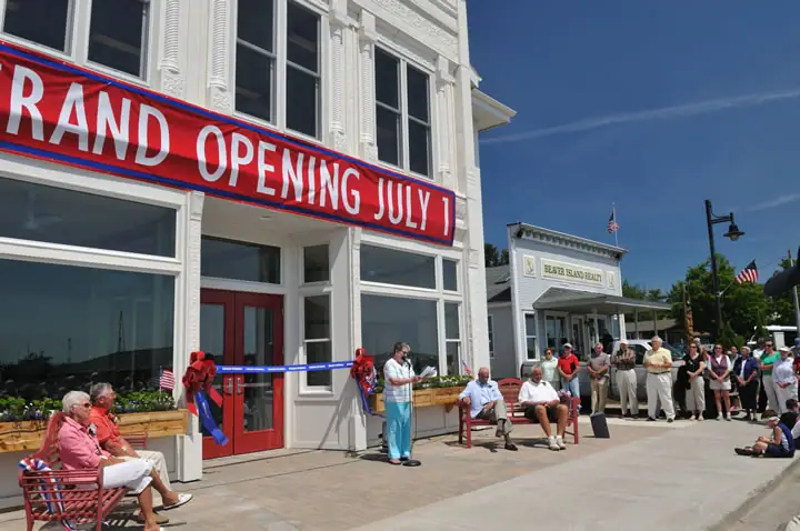 A speaker addresses a crowd outside a white building during a ribbon-cutting ceremony.