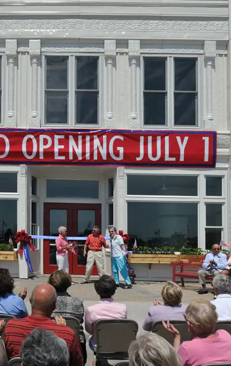 A ribbon-cutting ceremony takes place before a decorated building and a seated audience.