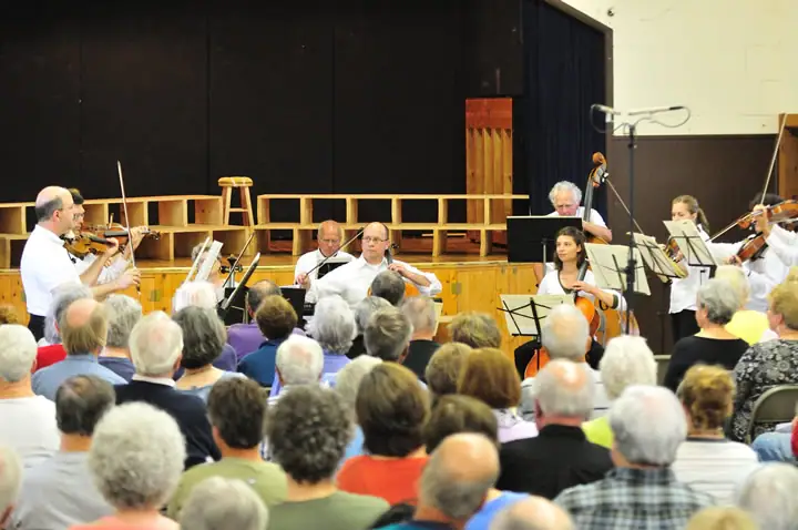String musicians perform on a stage before a seated audience.