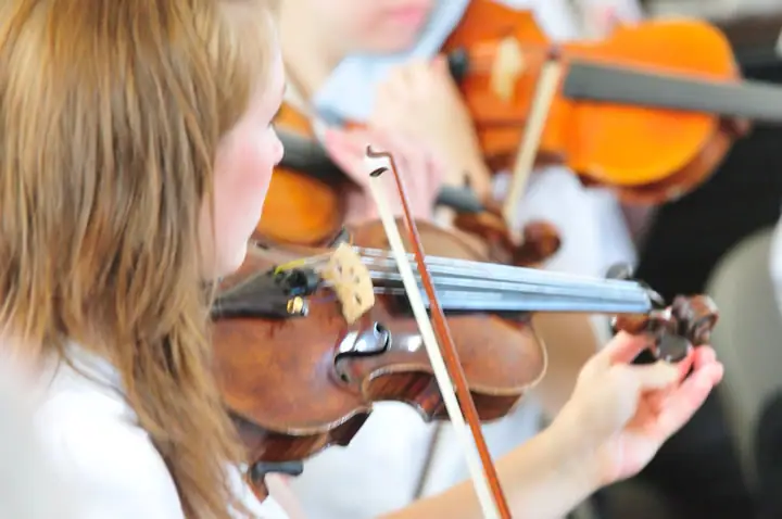 A child plays violin with other string musicians behind her.