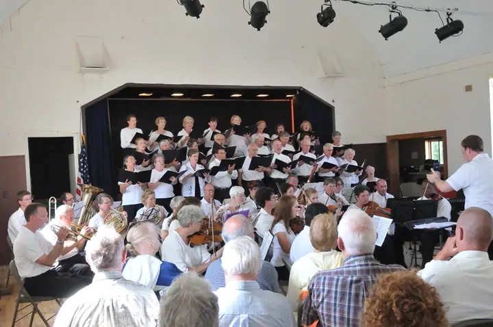 A choir and orchestra perform on a stage before a seated audience.