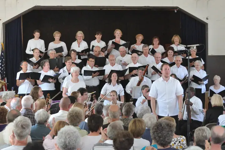 A choir and instrumental ensemble perform onstage before a seated audience.
