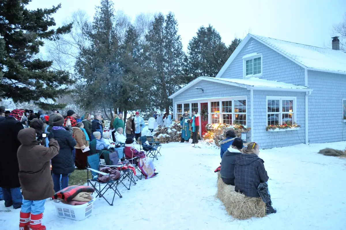 A winter gathering watches a costumed outdoor performance beside a shingled house.