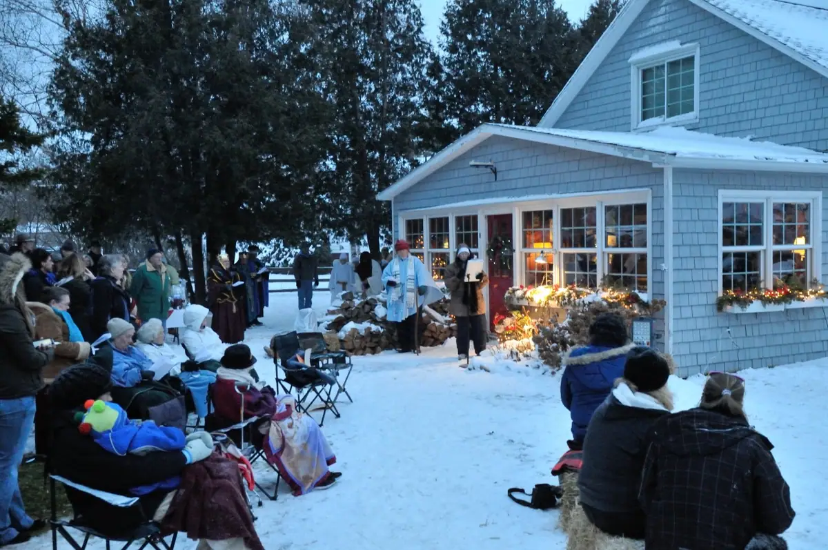 A winter outdoor gathering watches costumed performers beside a decorated shingled house.