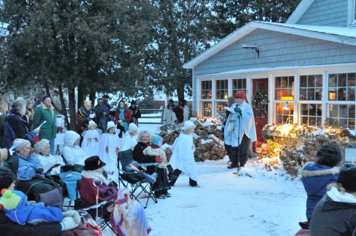 People gather for an outdoor nativity performance beside a snow-covered house.