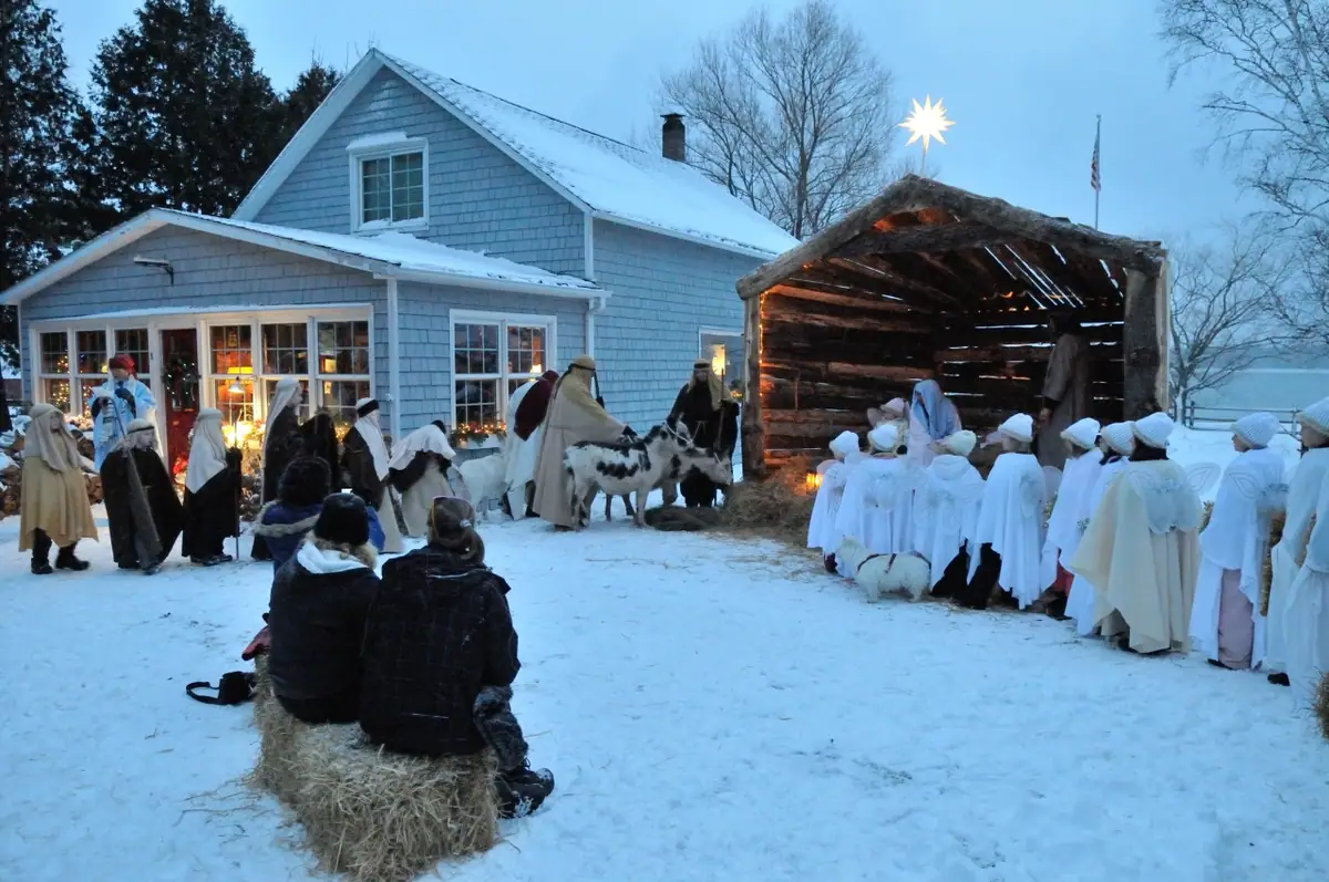 A costumed nativity scene unfolds in a snowy yard beside a blue shingled house.