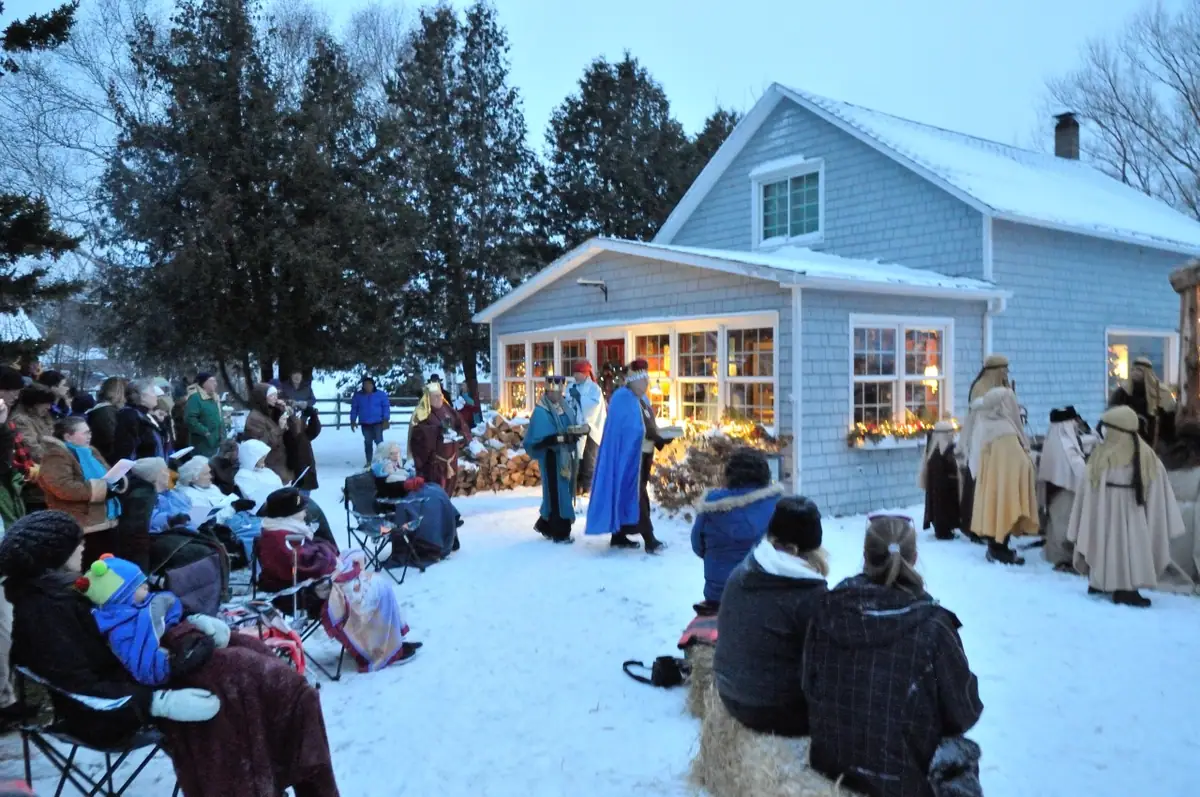 A winter audience watches costumed performers outside a snow-covered house.
