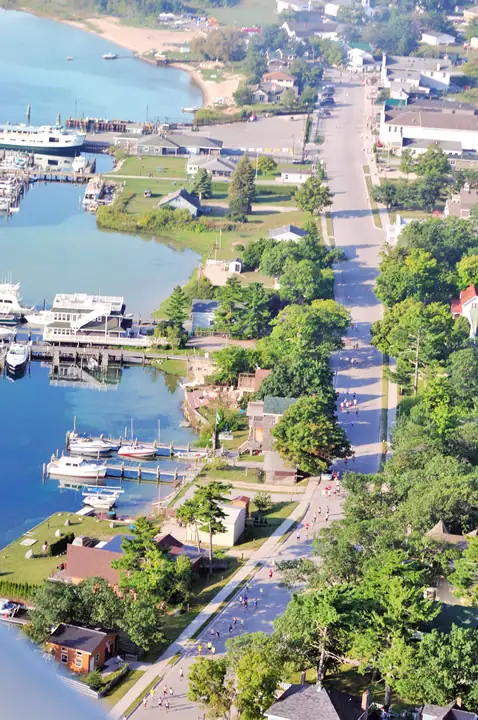 Aerial view of a waterfront street, docks, boats, buildings, and people gathered along a paved route.