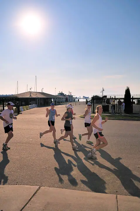 Five runners pass a waterfront harbor area in bright morning sunlight.