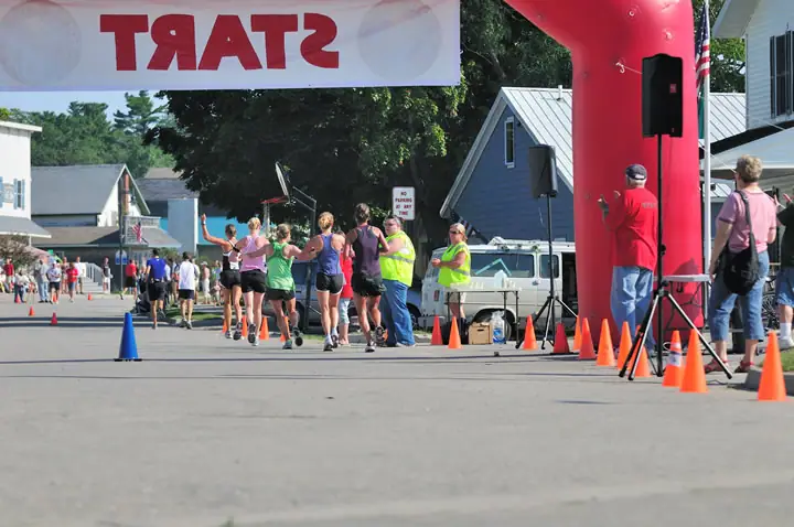 Runners pass beneath an inflatable arch on a street lined with traffic cones and spectators.