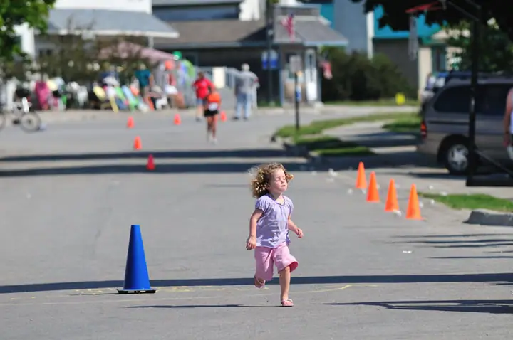 A child runs along a cone-marked street while people and storefronts blur in the background.