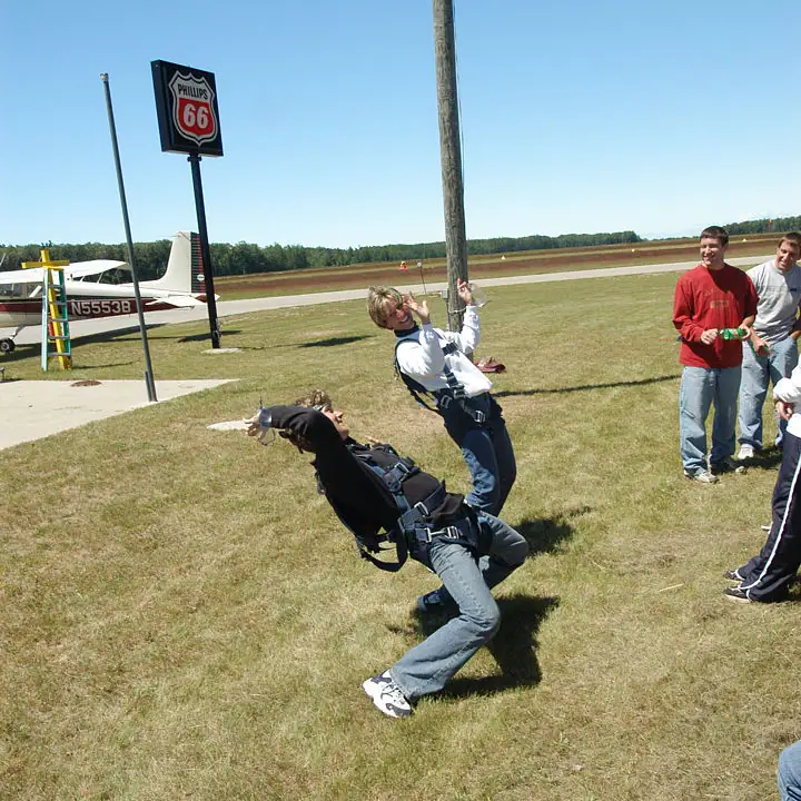 People demonstrate a harness activity beside a small airplane and runway, with a Phillips 66 sign in the background.