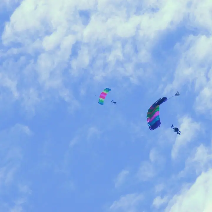 Two people descend beneath colorful parachute canopies against a cloudy blue sky.
