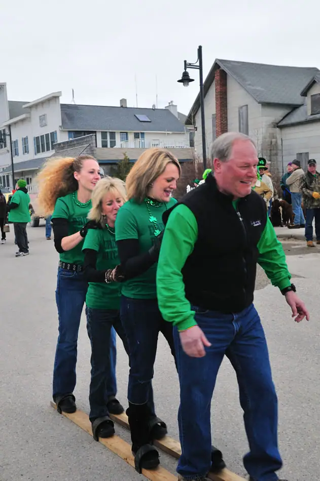 Adults in green clothing walk together on wooden planks during a street celebration.